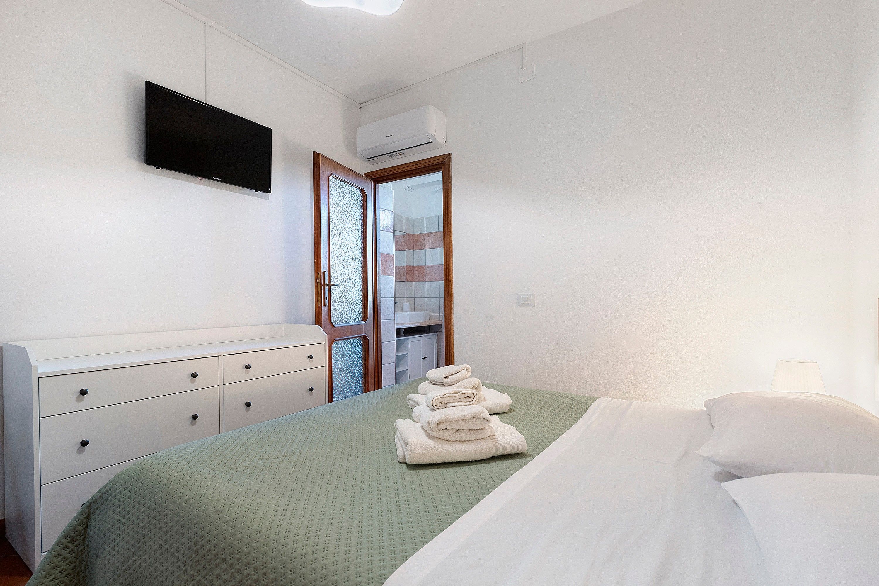 Ein Hotelzimmer mit einem Bett, einem an der Wand montierten Fernseher, einem Kleiderschrank und einer Klimaanlage.