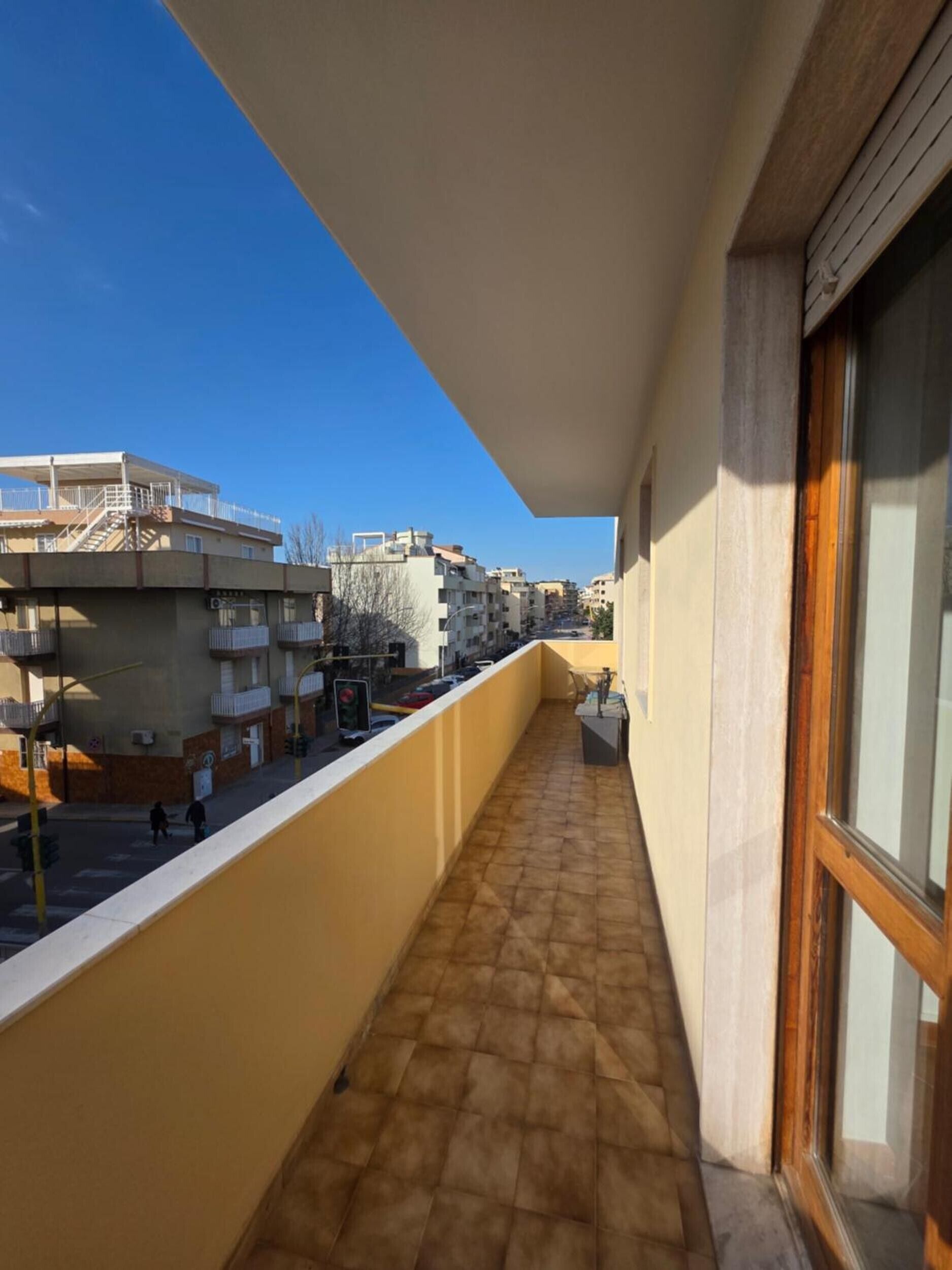 Ein Balkon mit Fliesenboden, Blick auf benachbarte Gebäude und einem wolkenlosen Himmel.