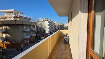 Ein Balkon mit Fliesenboden, Blick auf benachbarte Gebäude und einem wolkenlosen Himmel.