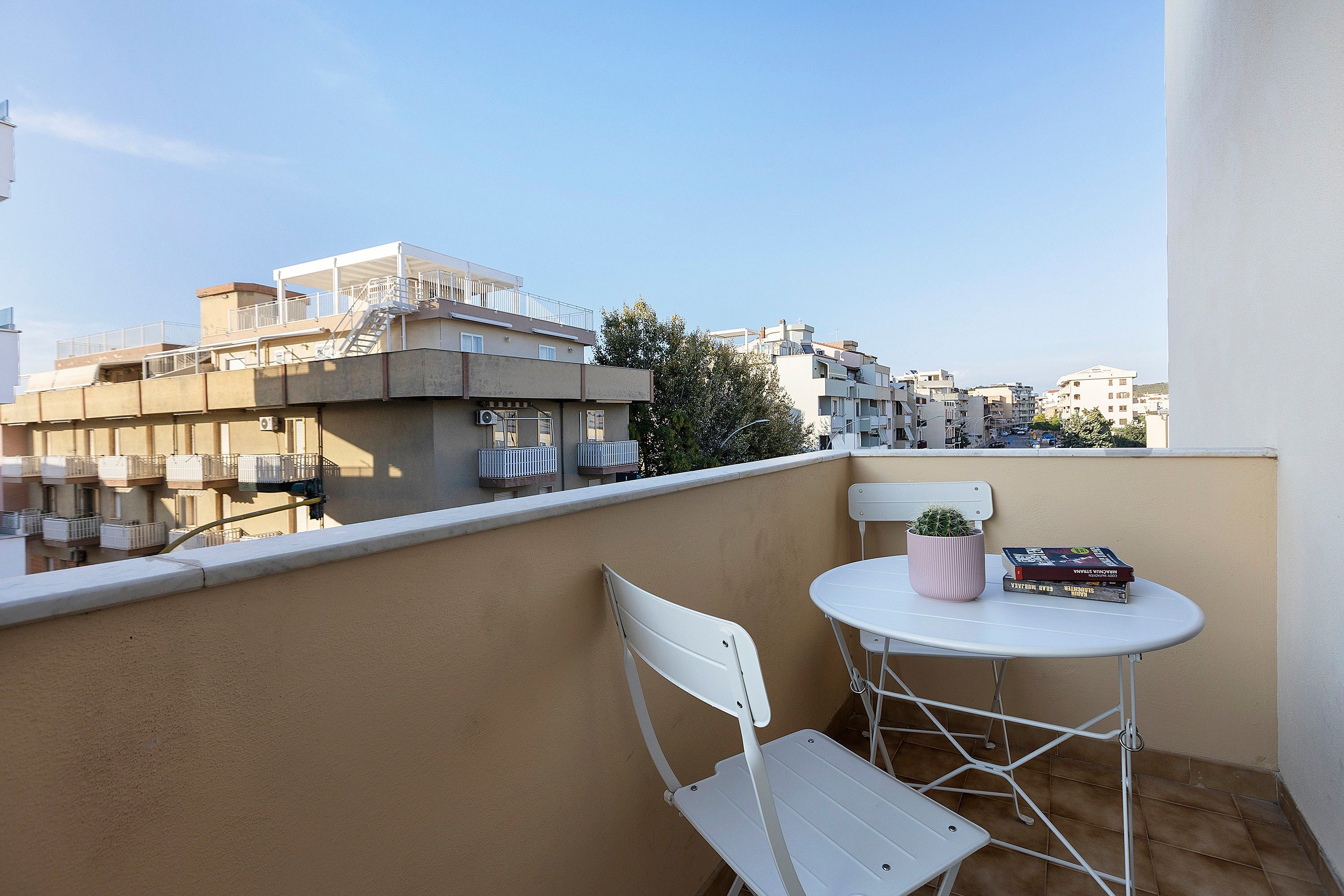 A balcony with a white chair and a small table, a potted plant, and a stack of books.