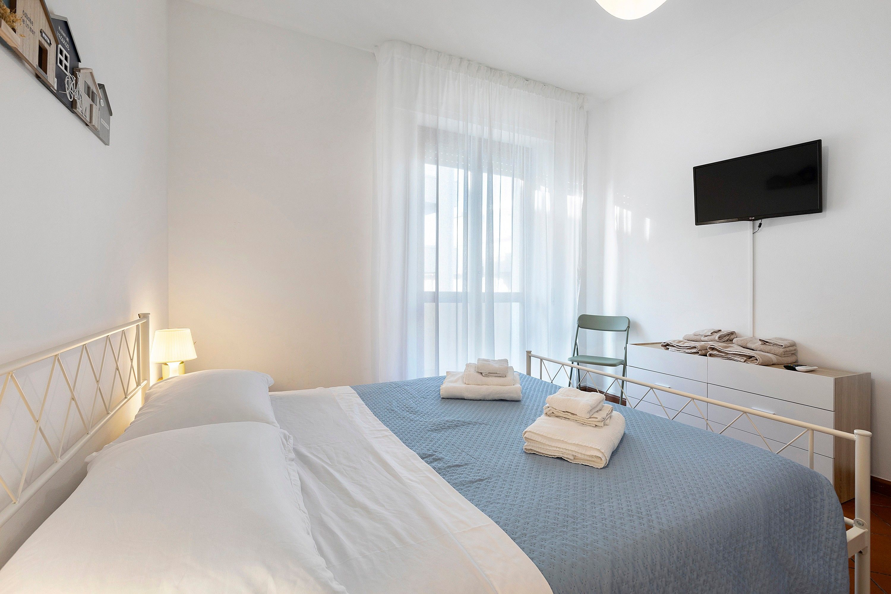 A bedroom with a bed, a television, a chair, and a window with curtains.