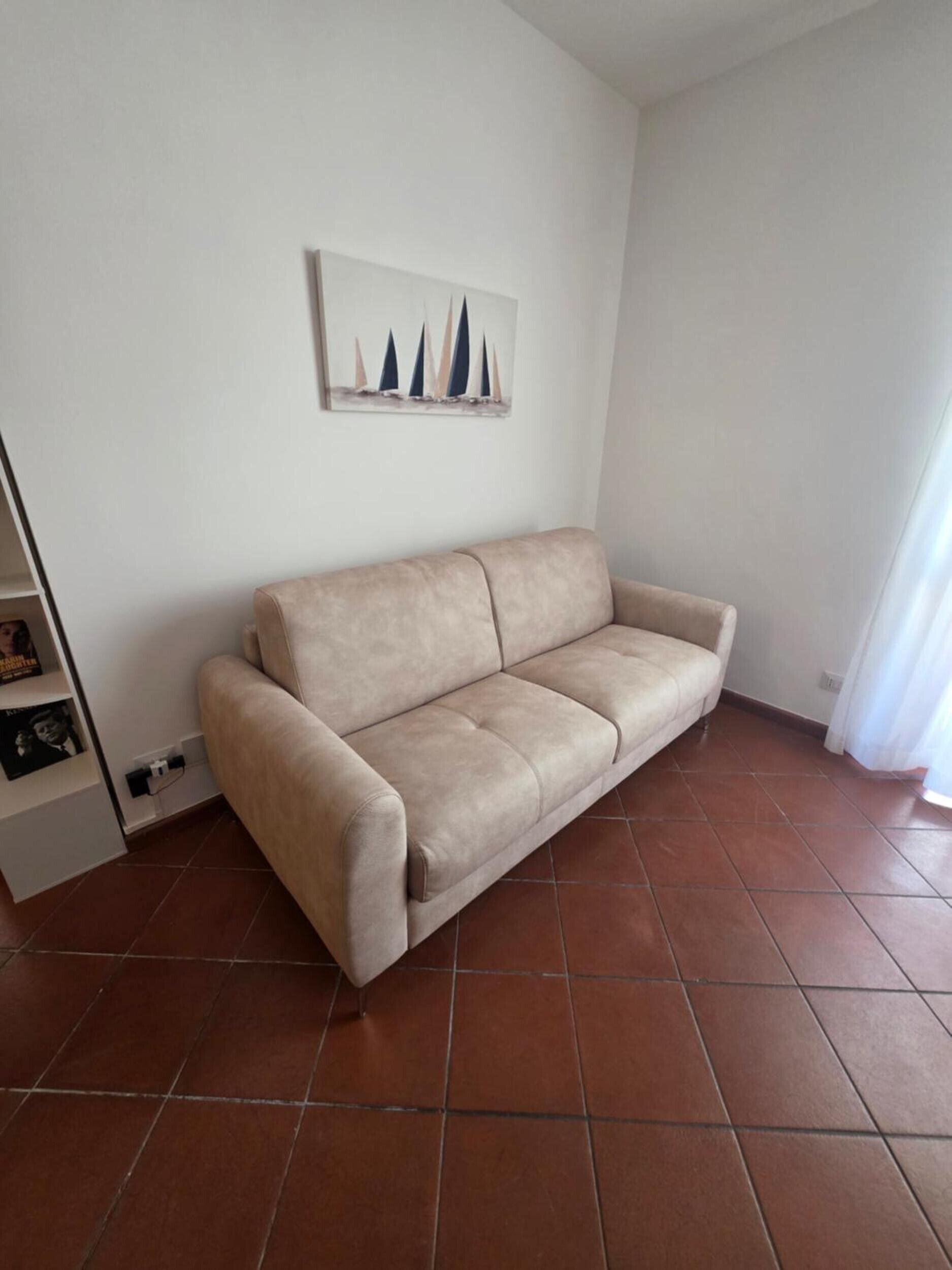 Ein Wohnzimmer mit einem beigen Sofa, einem Wandbild und einem Fliesenboden.