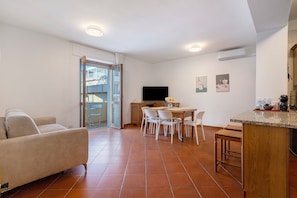 Un salon avec un canapé, un coin repas avec une table et des chaises, une cuisine avec un plan de travail et des appareils électroménagers, et un téléviseur fixé au mur.