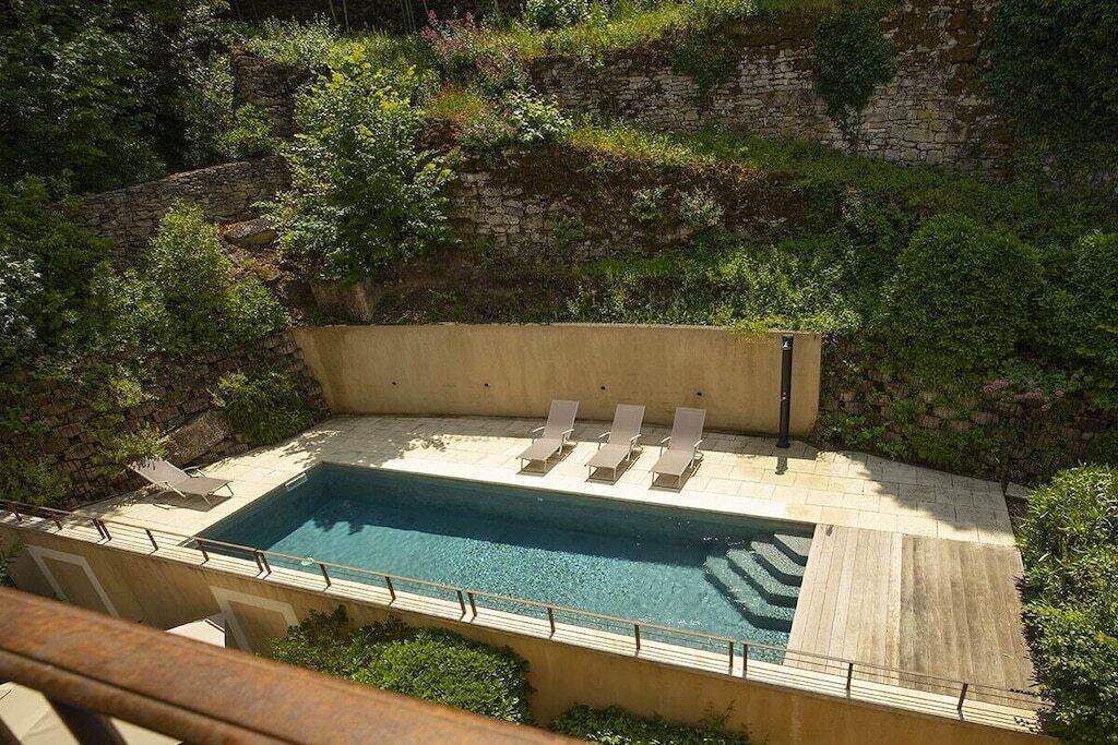 Una piscina rectangular con un muro de piedra y vegetación circundante.