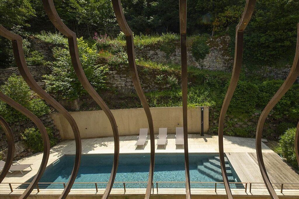 A swimming pool with lounge chairs and a stone wall in the background.