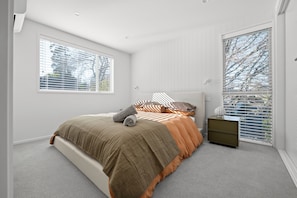 Een slaapkamer met een bed, een nachtkastje en een raam met jaloezieën.