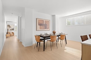 Een moderne eetruimte met een houten tafel, rieten stoelen en een eigentijds abstract schilderij.