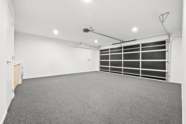Een garage met een grijze vloerbedekking, een witte deur en een plafondlamp.