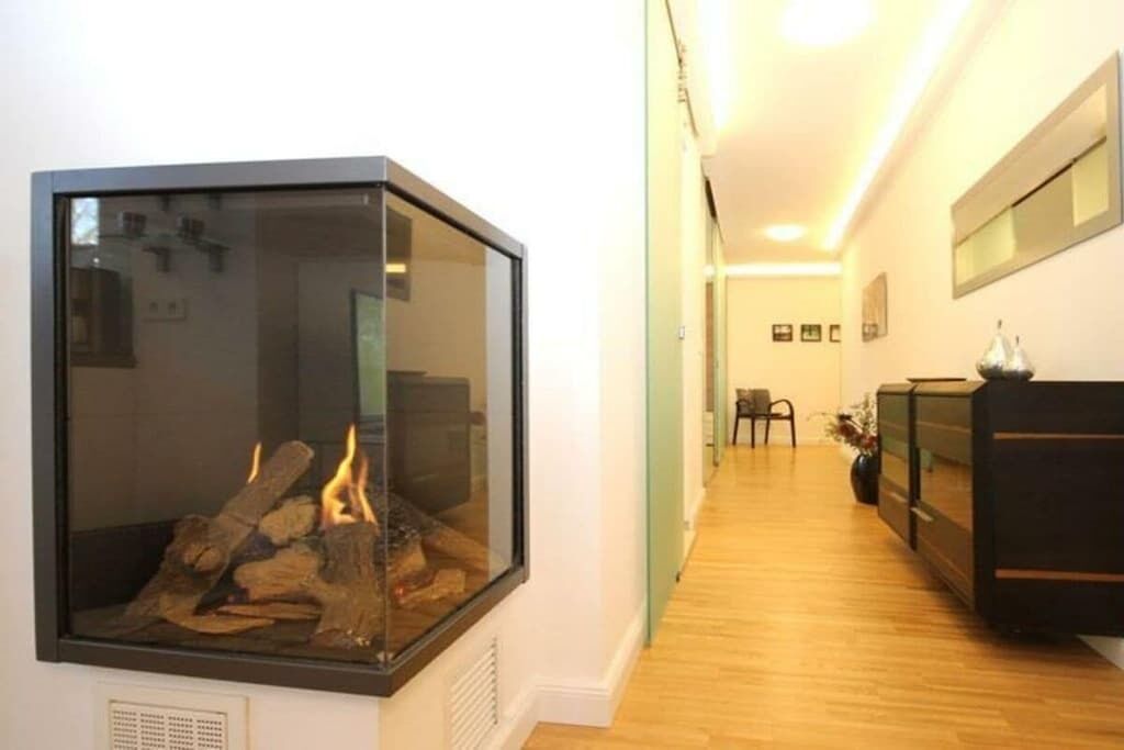 Ein Flur mit Kamin aus Glas, Holzboden, einem schwarzen Schrank und einem Stuhl.