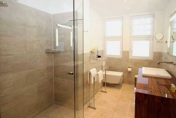Ein modernes Badezimmer mit einer gläsernen Duschkabine, einem Holzbadezimmerhocker und einer Toilette.