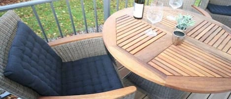 Mesa redonda de madera con dos sillas de mimbre, una botella de vino y dos copas en una terraza.