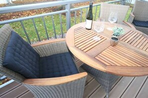Ein runder Holztisch mit zwei Korbstühlen, einer Weinflasche und zwei Gläsern auf einer Terrasse.