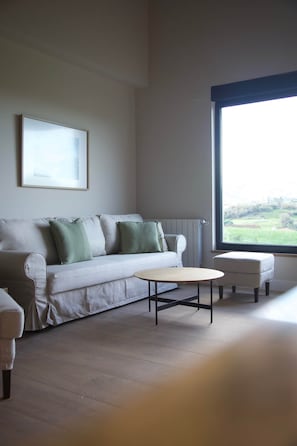 Ein minimalistisches Wohnzimmer mit einer Couch, einem Couchtisch und Blick auf eine grüne Landschaft durch ein großes Fenster.