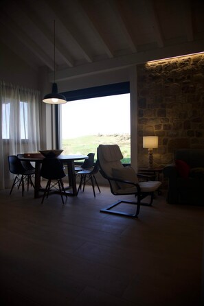 Ein Essbereich mit Tisch und Stühlen, einer Pendelleuchte, einer Steinwand und Blick durch ein Fenster.