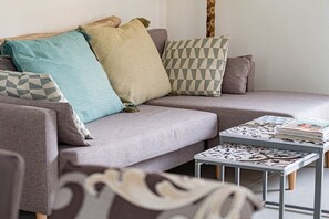 Ein modernes Wohnzimmer mit einem grauen Sofa, gemusterten Kissen und einem kleinen Beistelltisch mit einer Zeitschrift.