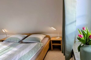 A bedroom with two beds, bedside tables, a lamp, and a vase with flowers. - Holiday home in Hooksiel with swimming pool (Hooksiel)