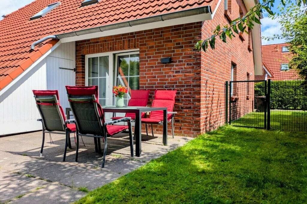 A brick house with a red tiled roof, a patio with a table and chairs, and a small garden area.