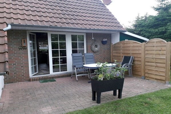 Une terrasse avec une table et des chaises, une clôture en bois et une maison en briques avec un toit en tuiles.