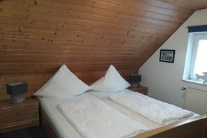 Quarto com teto de madeira, cama com travesseiros, mesa de cabeceira com alto-falante e janela com vista.