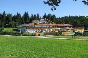 A two-story building with a balcony, surrounded by a green landscape and trees. - Holiday apartment with 2 bedrooms (Neureichenau)