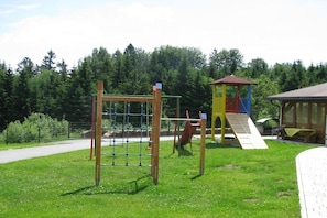 A playground with a climbing structure and a slide, surrounded by a grassy area and trees. - Holiday apartment with 2 bedrooms (Neureichenau)