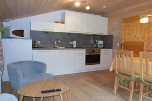 Ett kompakt kök med vita skåp, en mikrovågsugn, en kaffebryggare och ett litet matbord med stolar.