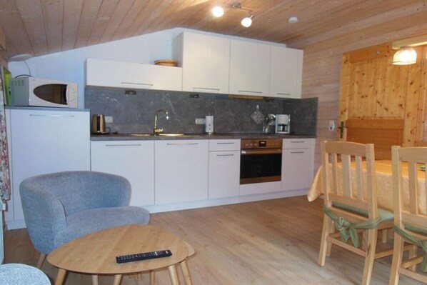 Een kleine keuken met witte kastjes, een magnetron, een koffiezetapparaat en een eettafel met stoelen.