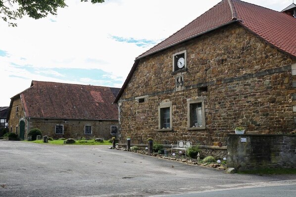 A stone building with a clock, a red-tiled roof, and a paved street. - White Horse Diedersen (Coppenbrügge)