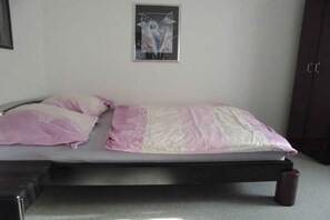 A single bed with a pink and white bedspread, a framed abstract artwork on the wall, and a dark-colored wardrobe.