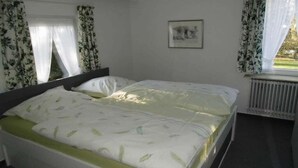 Une chambre à coucher avec un lit, des rideaux, un radiateur et un tableau encadré accroché au mur.