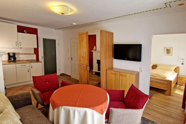 Ein kompakter Wohnraum mit einer Küchenzeile, einem Essbereich, einem an der Wand befestigten Fernseher und einem Bett.