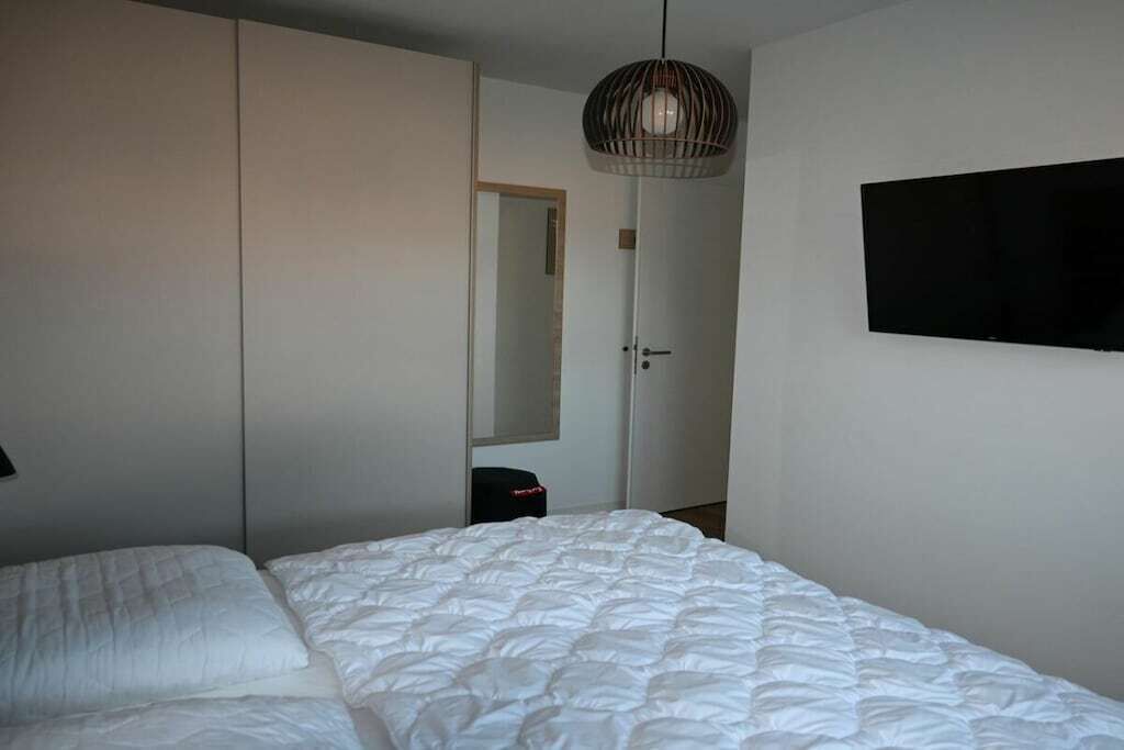 A bedroom with a bed, a wardrobe, a mirror, and a television on the wall.