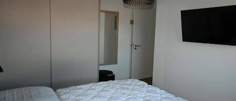 A bedroom with a bed, a wardrobe, a mirror, and a television on the wall.