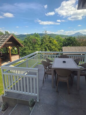 A patio with a table and chairs, a white railing, and a view of mountains. - Private Family House with Garden & Gazebo Sleeps 10 Sarajevo (Sarajevo)