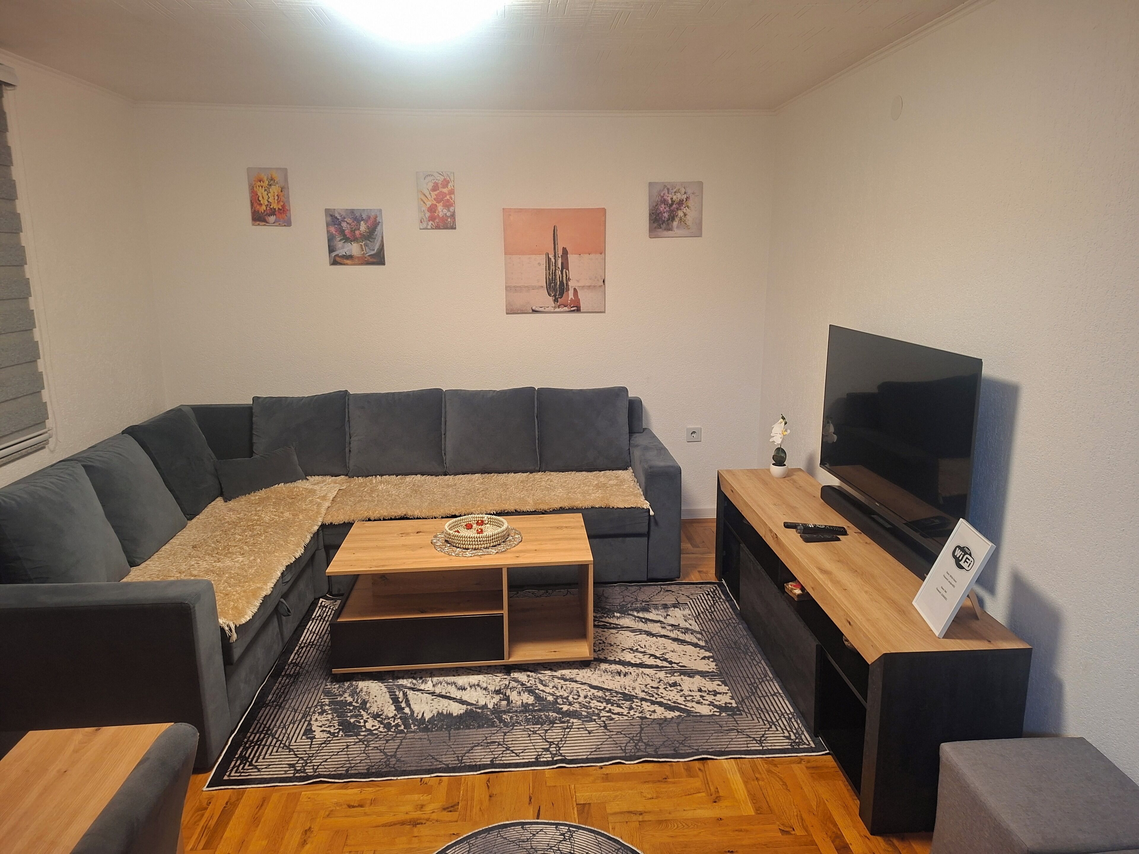 A modern living room with a sectional sofa, a flat-screen TV, a coffee table, and a decorative rug.