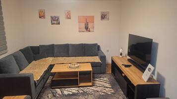 A modern living room with a sectional sofa, a flat-screen TV, a coffee table, and a decorative rug.