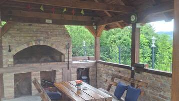 An outdoor patio with a brick fireplace, wooden benches, and a table with a vase of flowers.