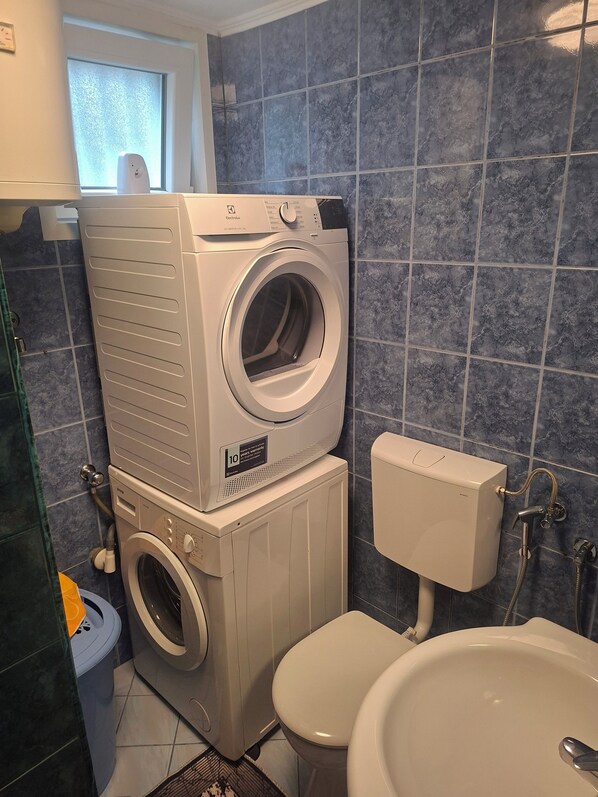 Een kleine badkamer met een gestapelde wasmachine en droger, een toilet en een wastafel.
