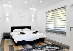 A modern bedroom with a bed, bedside tables, a window with blinds, and a patterned rug. - Private Family House with Garden & Gazebo Sleeps 10 Sarajevo (Sarajevo)