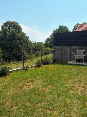 A grassy backyard with a stone building, a metal fence, and a bench. - Private Family House with Garden & Gazebo Sleeps 10 Sarajevo (Sarajevo)