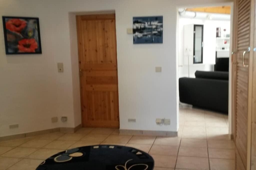 Una habitación con una puerta de madera, un tapete circular negro y dos cuadros colgados en la pared.