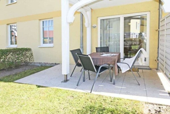 Un patio con mesa y sillas, un área de estar techada y un ventanal corredizo.