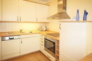 A kitchen with white cabinets, a dishwasher, an oven, a coffee maker, and a refrigerator. - Holiday apartment Residence Ostseestrand 319619 (Kühlungsborn)