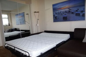 A bedroom with a bed, a sofa, a large mirror, and a painting of a beach scene. - Villa Parkblick Apt. 17 (Kühlungsborn)