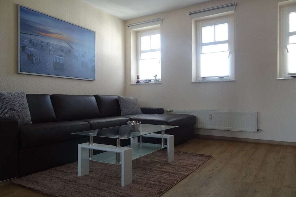 Een woonkamer met een zwarte bank, een glazen salontafel en een schilderij aan de muur.