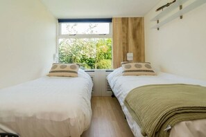 A bedroom with two beds, a window with a view of greenery, and a wooden wall panel. - "t Ongerepte 56 - De Zandbank (Renesse)