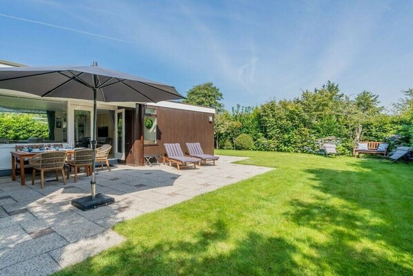 A patio with a table and chairs, a covered seating area, and a grassy lawn. - "t Ongerepte 56 - De Zandbank (Renesse)