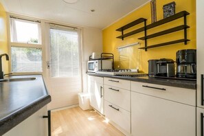Una cocina compacta con gabinetes blancos, una encimera negra y una ventana con persianas.