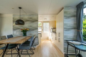 A modern kitchen with a marble backsplash, a dining area with a wooden table and chairs, and a view of the outdoors. - "t Ongerepte 56 - De Zandbank (Renesse)