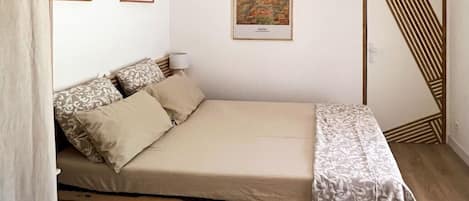 Una cama individual con estructura de madera, una manta estampada y dos almohadas.